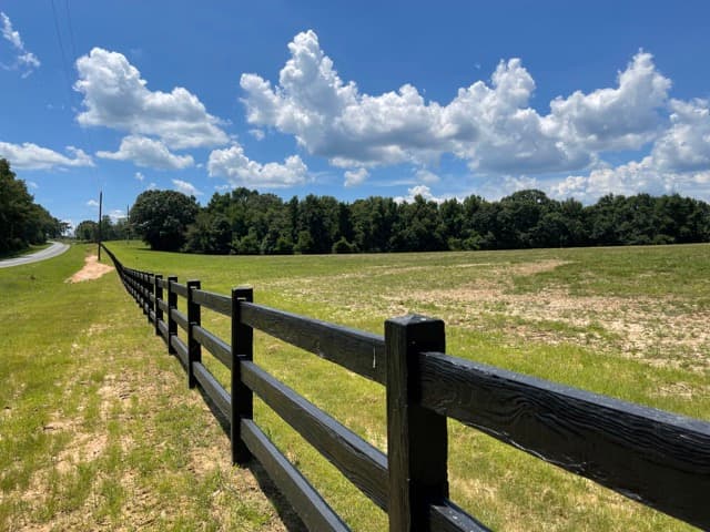Concrete ranch rail fence with wood-grain texture along a Florida property line, showing 3-rail configuration in natural wood color